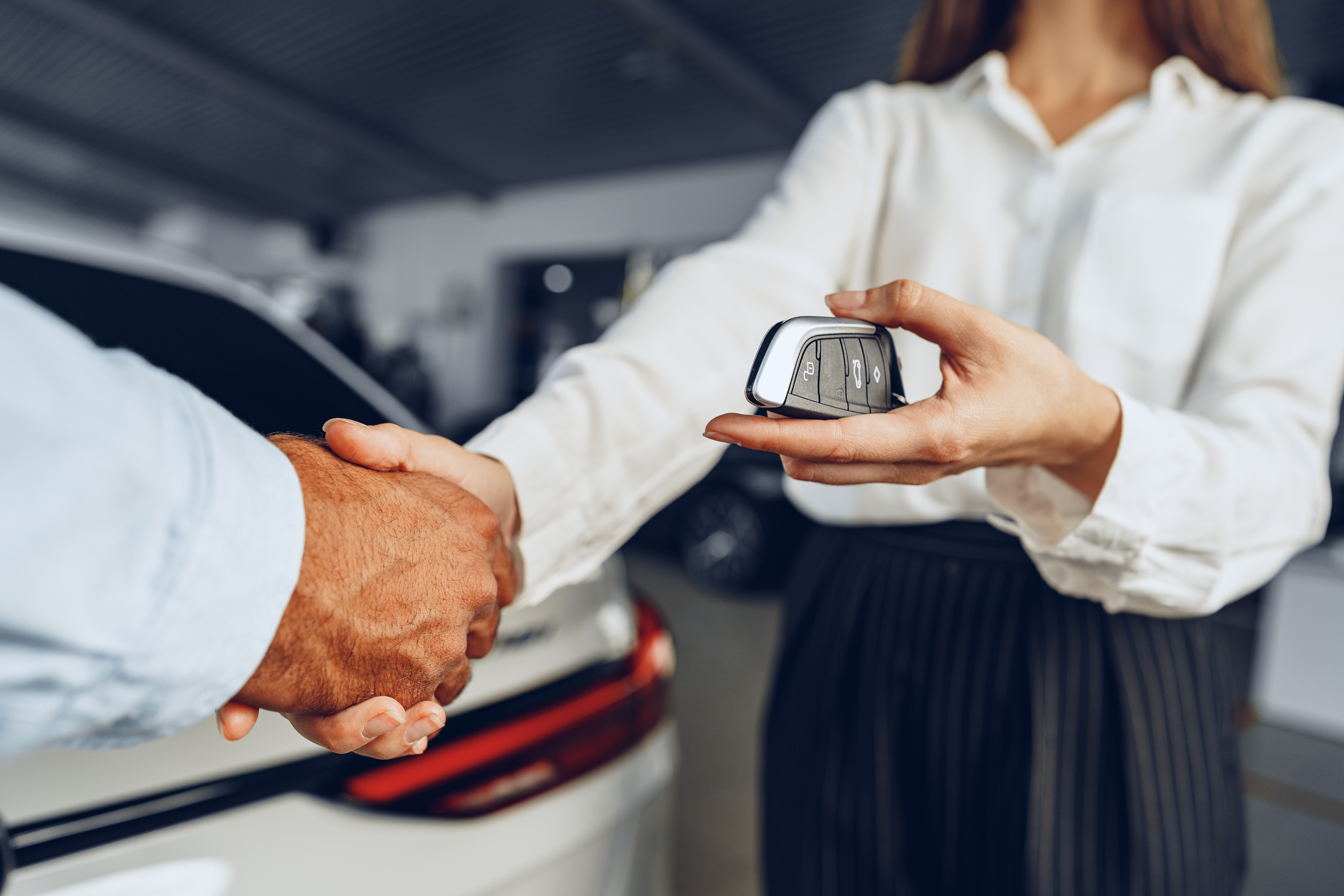Car seller and buyer handshake at car dealership against a new car
